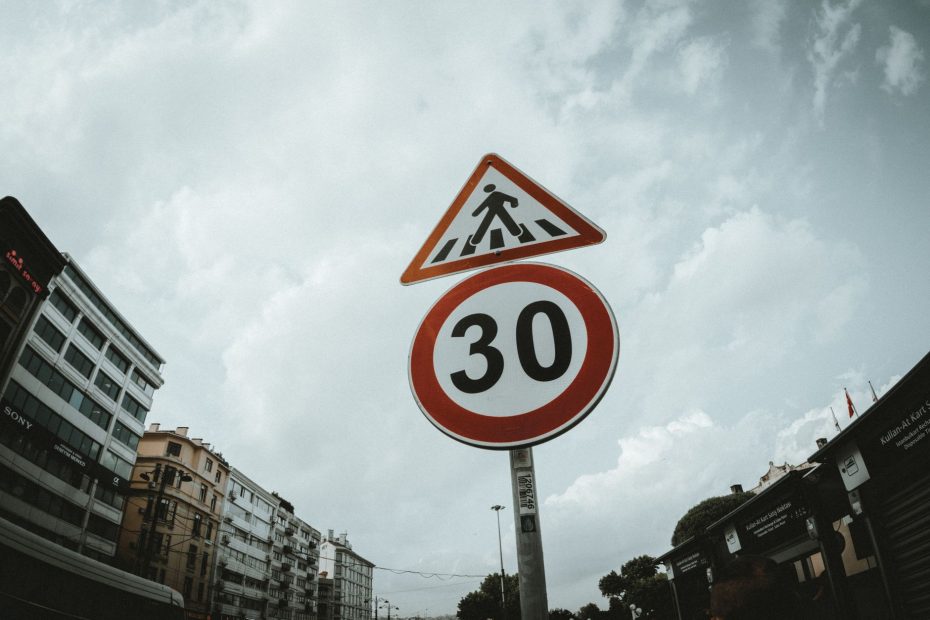 Low-angle view of pedestrian and speed limit signs against a cloudy sky in an urban setting.